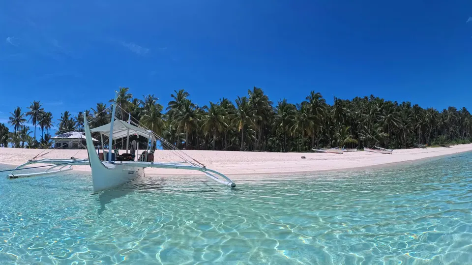 Barca tradicional filipina en una playa de arena blanca con palmeras y agua transparente