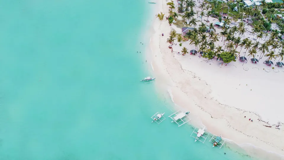 Vista aérea de una lengua de arena blanca y aguas turquesas en Filipinas con barcos tradicionales.